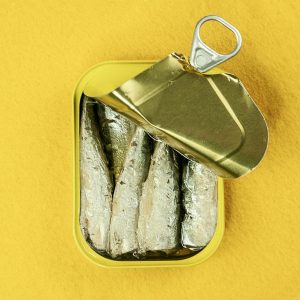 Metal can of sardines opened, revealing fish against a bright yellow background.