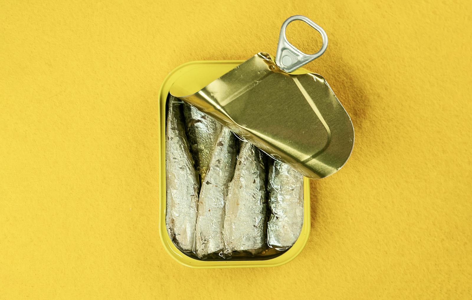 Metal can of sardines opened, revealing fish against a bright yellow background.