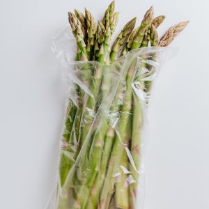 Bundle of fresh organic asparagus wrapped in a plastic bag on a white background.