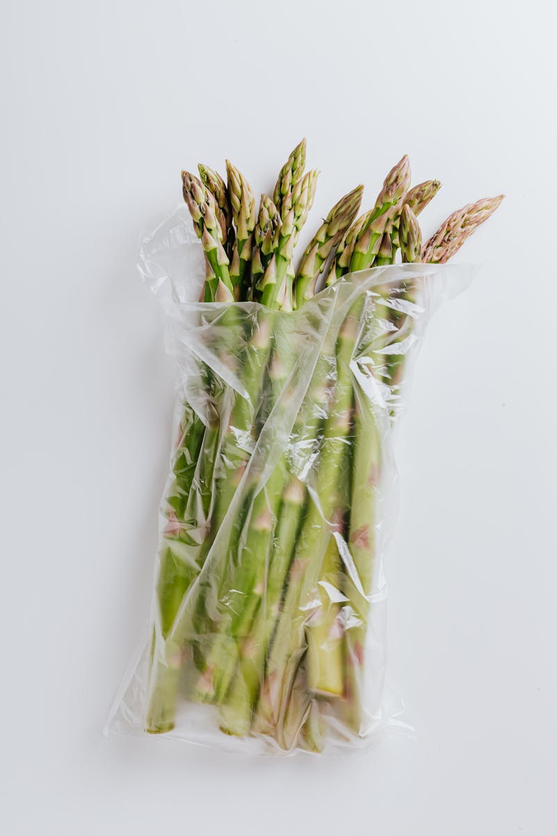 Bundle of fresh organic asparagus wrapped in a plastic bag on a white background.